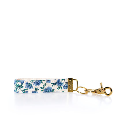 The Rustic Marlin Keychain - Blueberry by Rustic Marlin features blue floral patterns on fabric, gold hardware, and a lobster clasp, shown against a white background—an ideal chic bag charm or blueberry keychain to elevate your accessories.