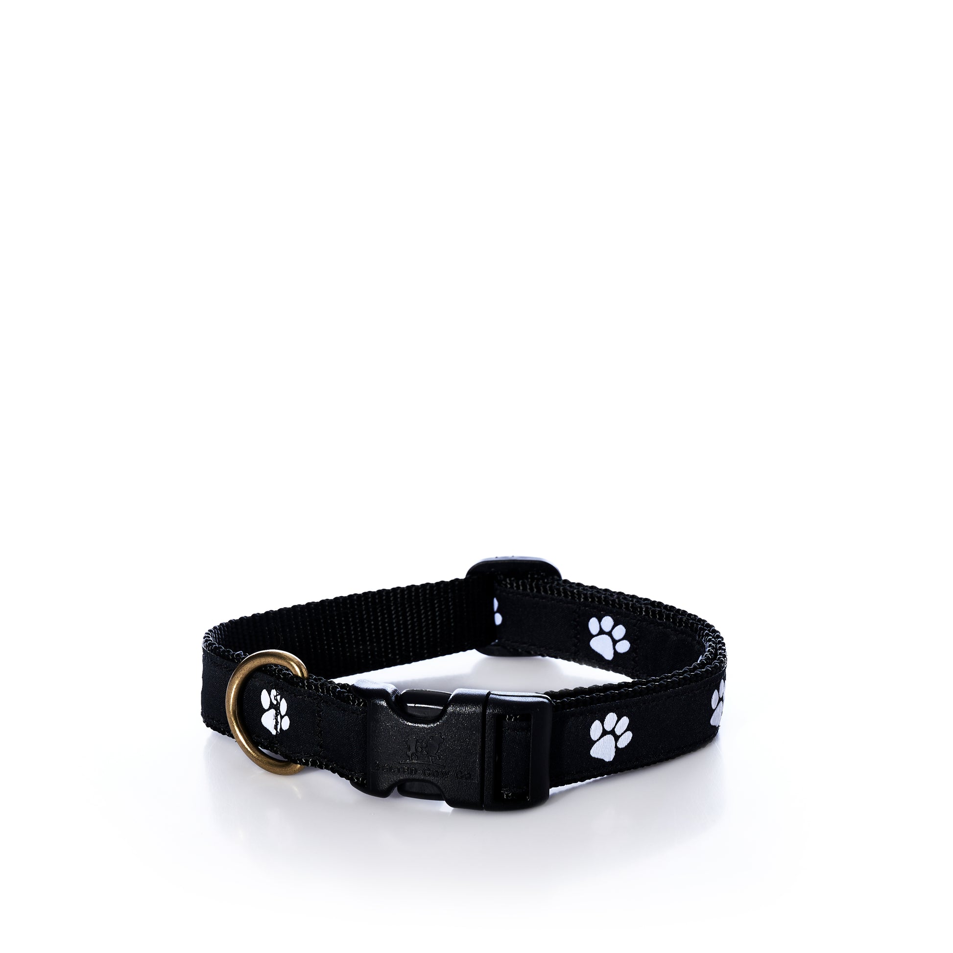 The Belted Cow Paw Print Dog Collar 1″ - Medium is crafted from durable black nylon webbing, features a plastic buckle, sturdy metal ring, and is decorated with a white paw print pattern, shown on a white surface.