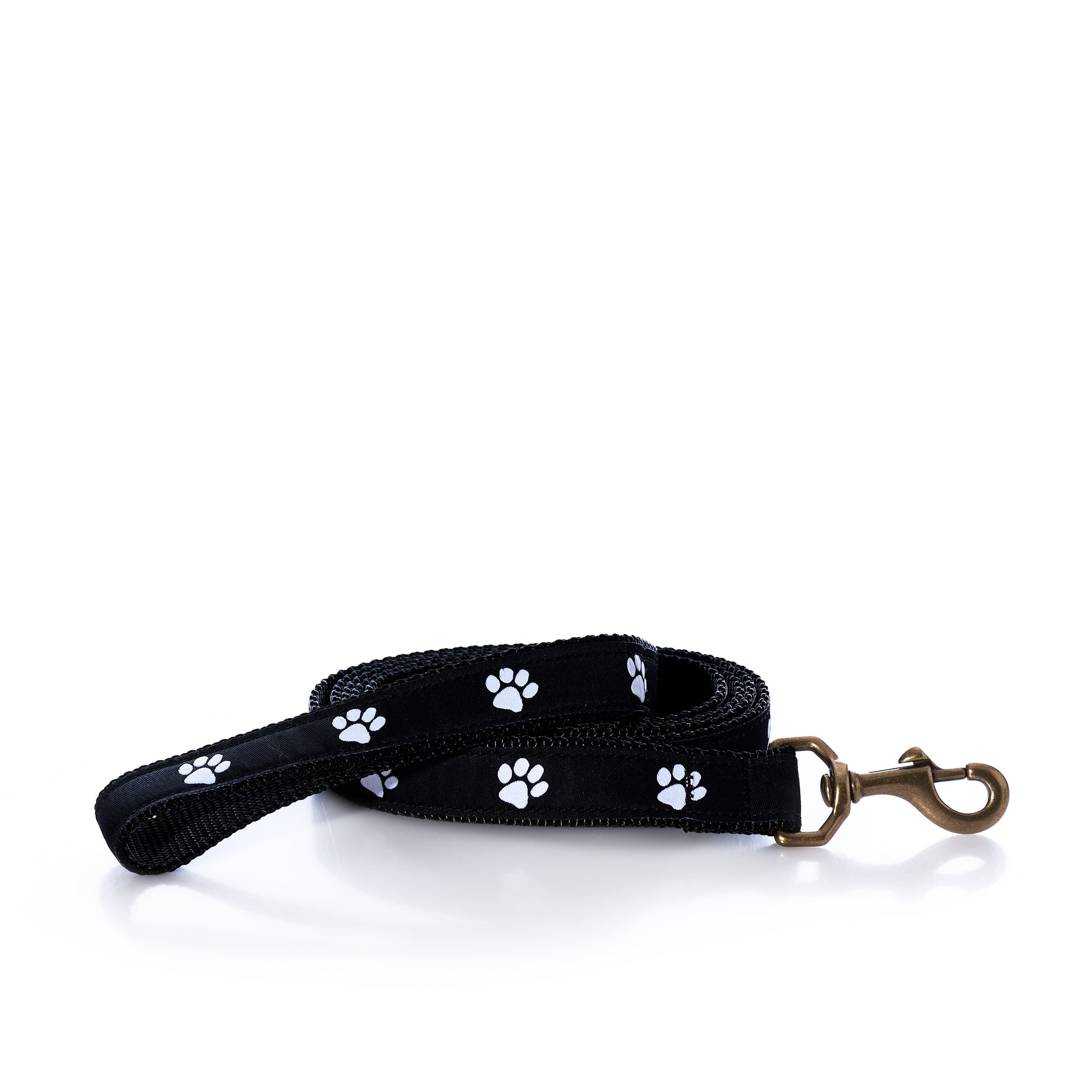 The Belted Cow Paw Print Dog Leash, featuring a black design with white paw prints and a robust metal clip, is coiled neatly on a white background.