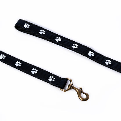Paw Print Dog Leash made of black heavy-duty nylon with a white paw print pattern and a brass-colored metal swivel snap hook.