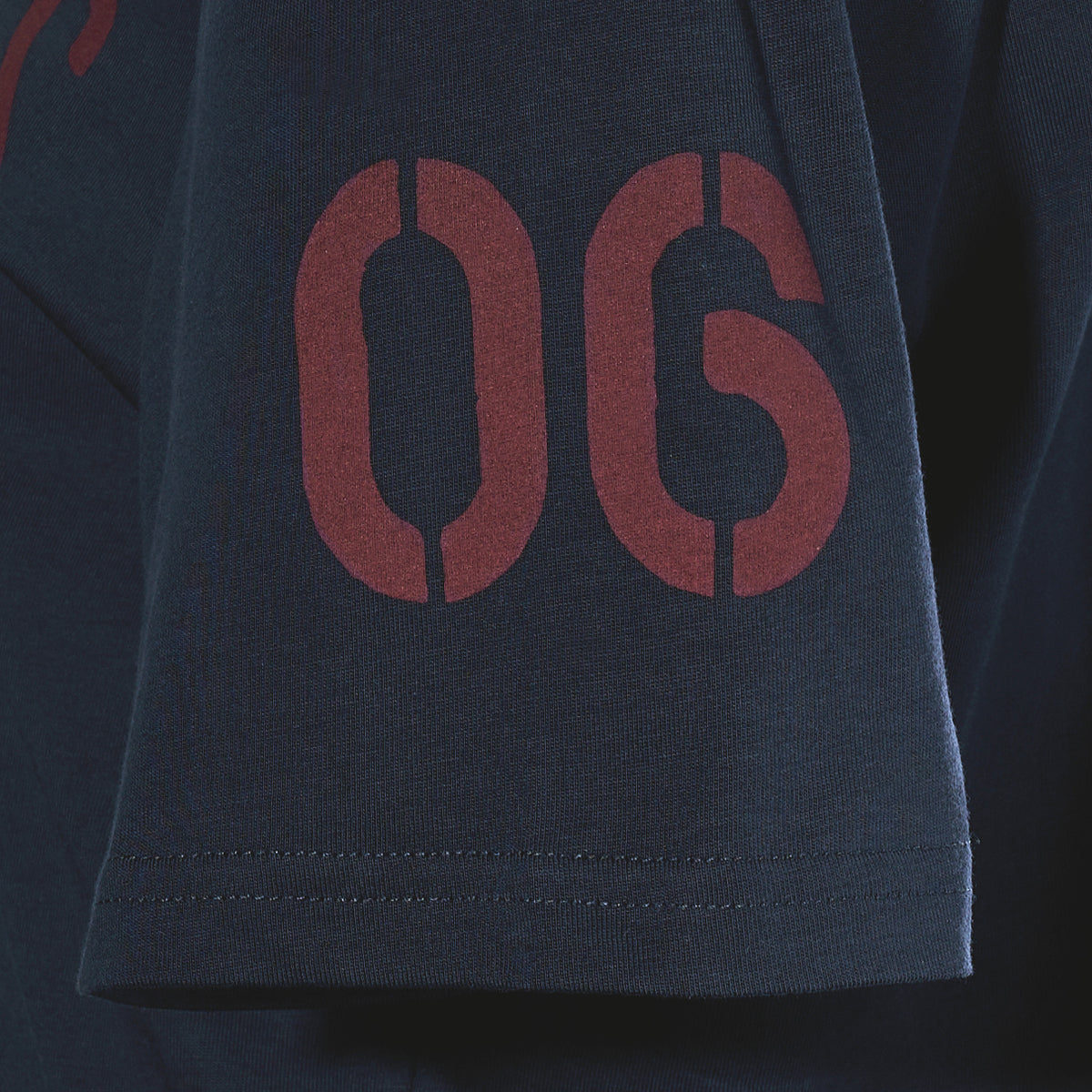 Dark blue sleeve of a Sea Bags Sailing Team T-Shirt featuring large dark red numerals 06 in a stencil font.