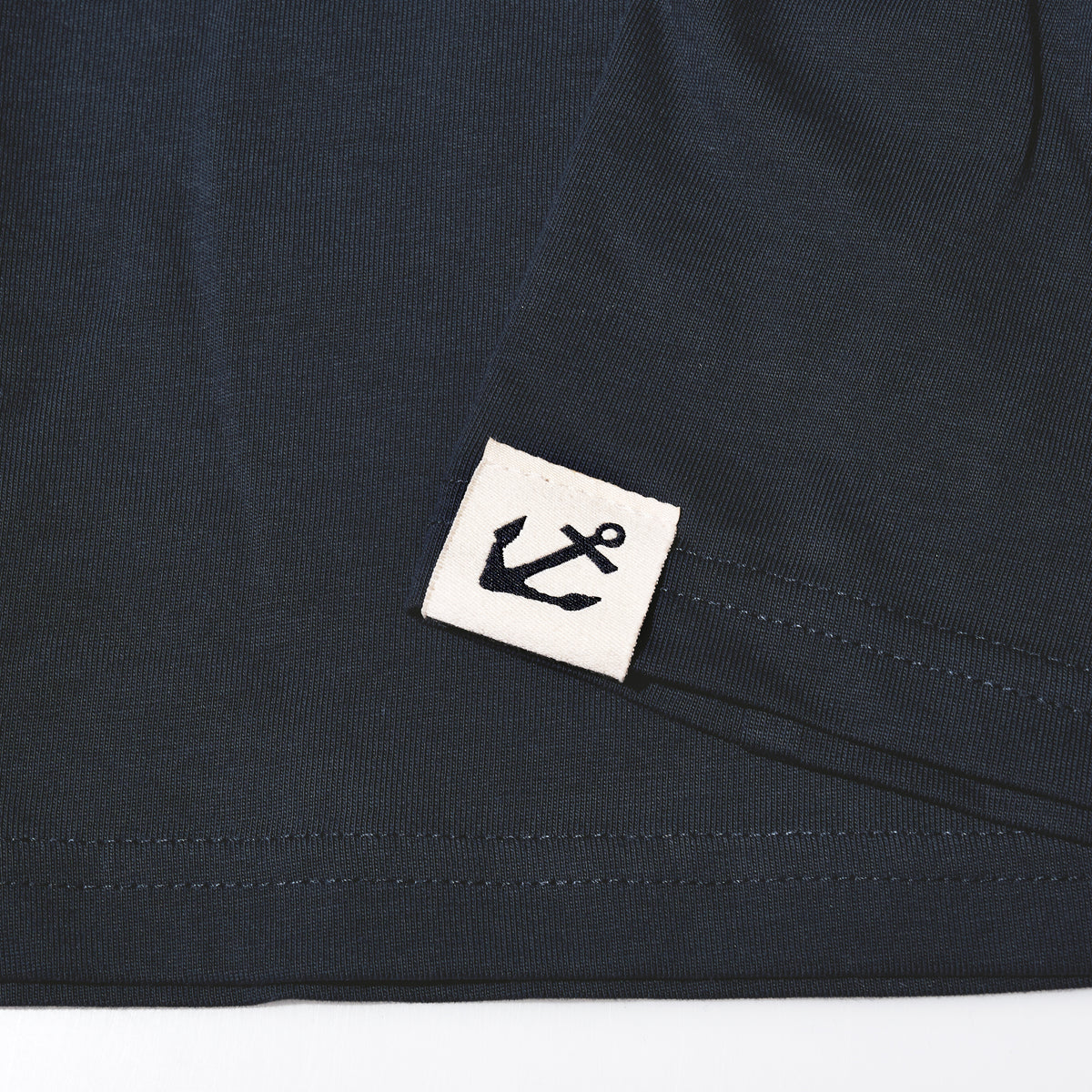 Dark navy Sea Bags Sailing Team T-Shirt with a small square tag featuring a black anchor icon at the hem.
