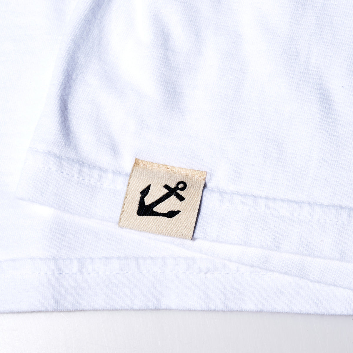 Salty Wharf Seagull T-Shirt hem with a small beige fabric tag featuring a black anchor icon.