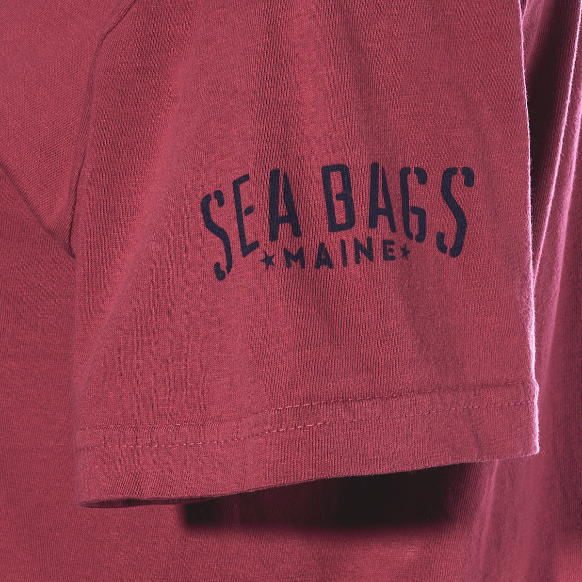 Maroon East Coast Shark T-Shirt sleeve featuring the text “SEA BAGS” above “MAINE.”