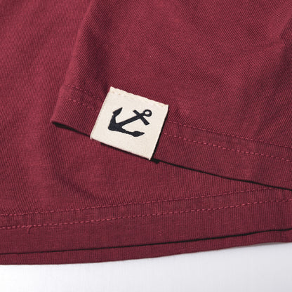 Maroon hem of the East Coast Shark T-Shirt featuring a small off-white tag with a black anchor icon, highlighting a nautical heritage style.