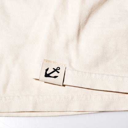 Off-white ringspun cotton hem of a Maine Sailing Team T-Shirt, featuring a small fabric tag with a black nautical anchor icon.