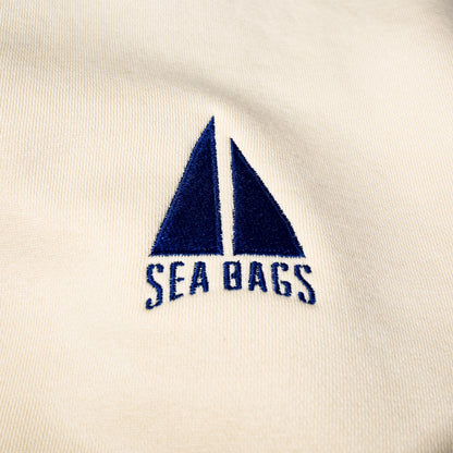 Cream-colored Sailboat Crewneck Sweatshirt featuring an embroidered dark blue sailboat icon above the text “SEA BAGS.”