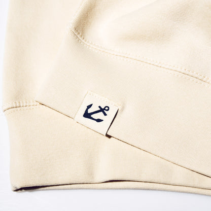 Close-up of a beige cotton sleeve hem on a Sailboat Crewneck Sweatshirt featuring a small square tag with a navy blue anchor icon.