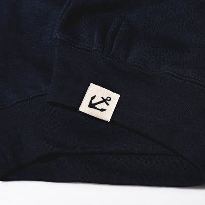 Dark blue Sea Bags Sailing Team Hoodie sleeve with a small cream-colored tag on the cuff featuring a Sea Bags anchor icon.