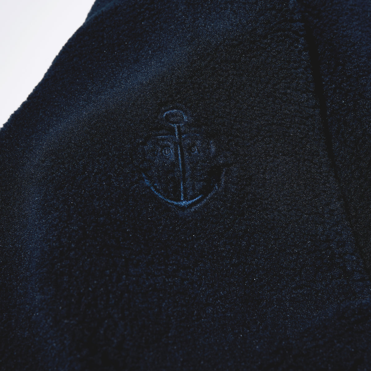 Close-up of the Fleece Button-Front Coat - Navy by Batela USA Inc, featuring a central embroidered anchor—ideal for coastal adventures.