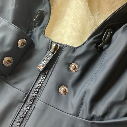 Close-up of the Harborside Waterproof Fleece-Lined Raincoat - Navy by Batela USA Inc, featuring metal snaps, zipper, and “ARENA” pull tab on a light textured background.