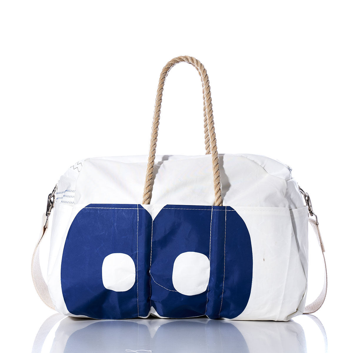 Sea Bags’ Vintage 58 Weekender features a white duffle design with blue and white circular patterns, tan rope handles, and a white shoulder strap. Displayed on a reflective surface, its the ideal companion for your next getaway. by Sea Bags