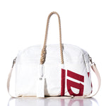 The Sea Bags Vintage Ideal18 Weekender—a white duffel bag featuring rope handles, a detachable shoulder strap, and a bold red graphic print on one side—is showcased on a reflective surface with a white background. by Sea Bags