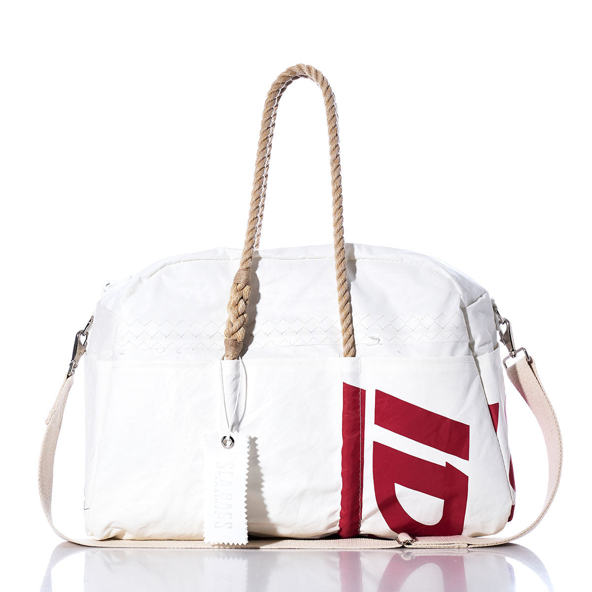 The Sea Bags Vintage Ideal18 Weekender—a white duffel bag featuring rope handles, a detachable shoulder strap, and a bold red graphic print on one side—is showcased on a reflective surface with a white background. by Sea Bags