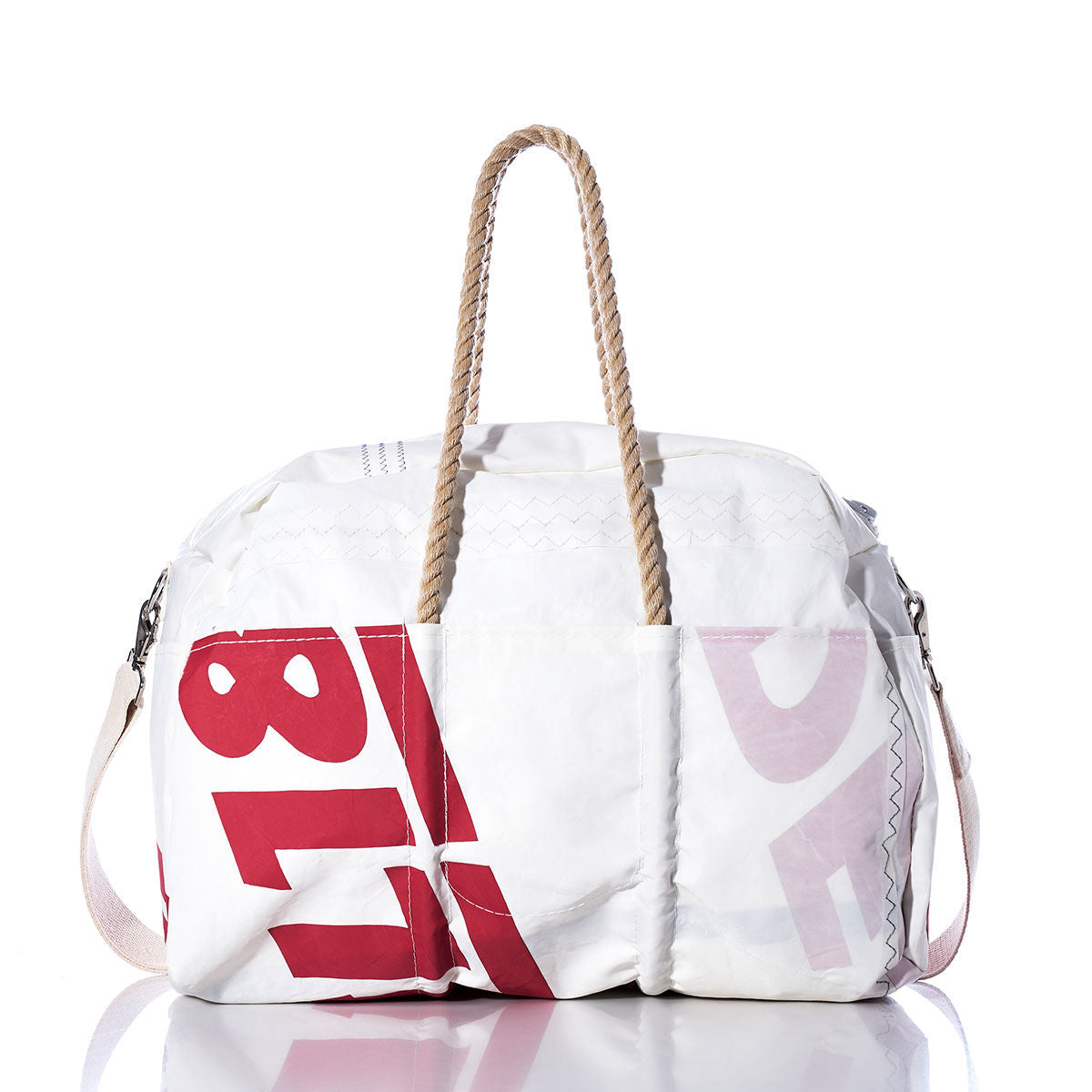 The Vintage Ideal18 Weekender by Sea Bags, a white and red bag with rope handles and side strap, features large printed numbers and letters and is photographed on a reflective surface. by Sea Bags