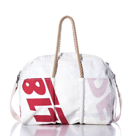 The Vintage Ideal18 Weekender by Sea Bags, a white and red bag with rope handles and side strap, features large printed numbers and letters and is photographed on a reflective surface. by Sea Bags