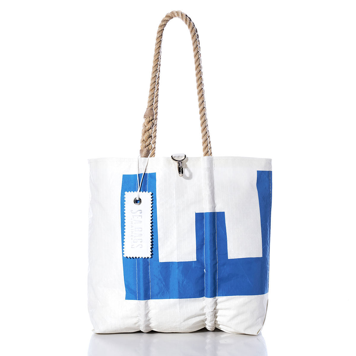 The Sea Bags Vintage Blue E Medium Tote features a blue geometric design on white sailcloth, hand-spliced rope handles, and a white tag near the top. This Maine-crafted tote stands upright against a white background. by Sea Bags