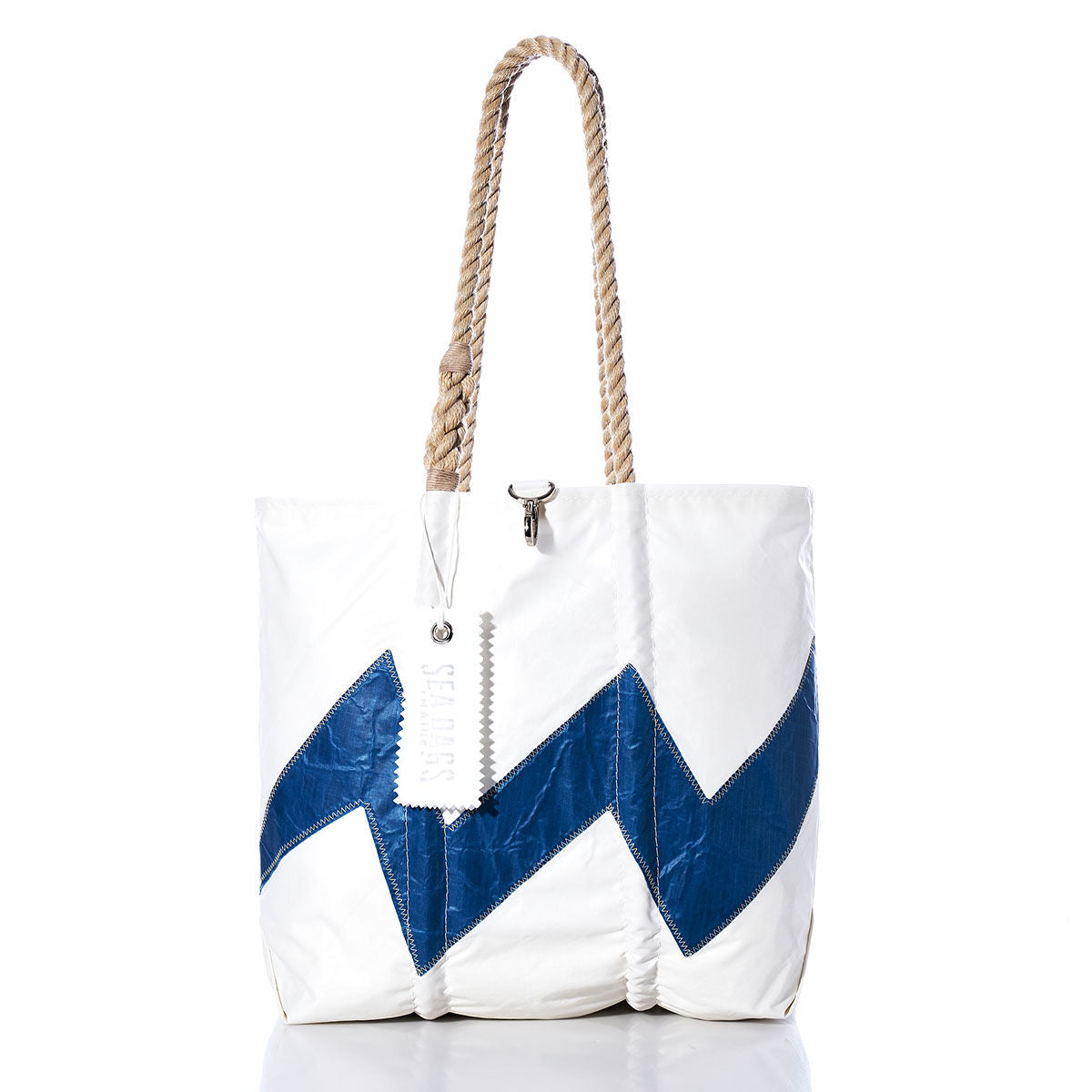 Sea Bags’ Vintage Lightning Medium Tote is a white tote bag accented with a blue zigzag pattern, hand-spliced rope handles, and an authentic sail insignia on the white tag. Displayed on a white background, this bag effortlessly combines nautical charm with timeless style. by Sea Bags