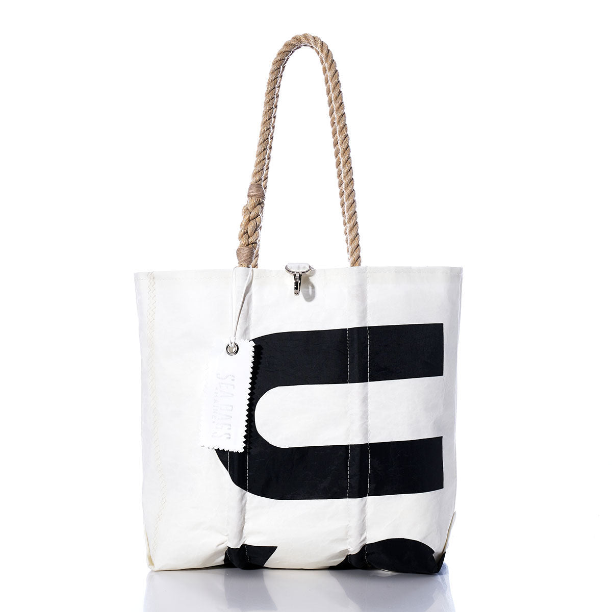 The Sea Bags Vintage US-8 Medium Tote features a white canvas body with a bold black letter graphic, hand-spliced rope handles, and an attached white tag. Inspired by classic Maine sail totes and photographed on a clean white background, this bag embodies the enduring charm and craftsmanship of Maine-made accessories. by Sea Bags