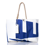 Sea Bags’ Vintage Etchells Large Tote is a spacious white tote bag featuring a striking blue geometric design, sturdy rope handles, and a distinctive white tag hanging from one handle. Made from durable sailcloth for lasting style, this handmade Maine bag is perfect for everyday use and beautifully showcased against a clean white background. by Sea Bags
