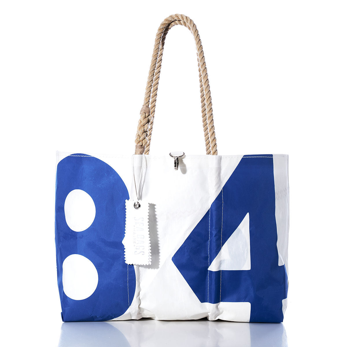 The Sea Bags Vintage 84 Large Tote, crafted from white and blue sail material with the number 84, features hand-spliced rope handles and a white tag, all showcased on a white background—evoking the timeless style of classic Maine handcrafted bags. by Sea Bags