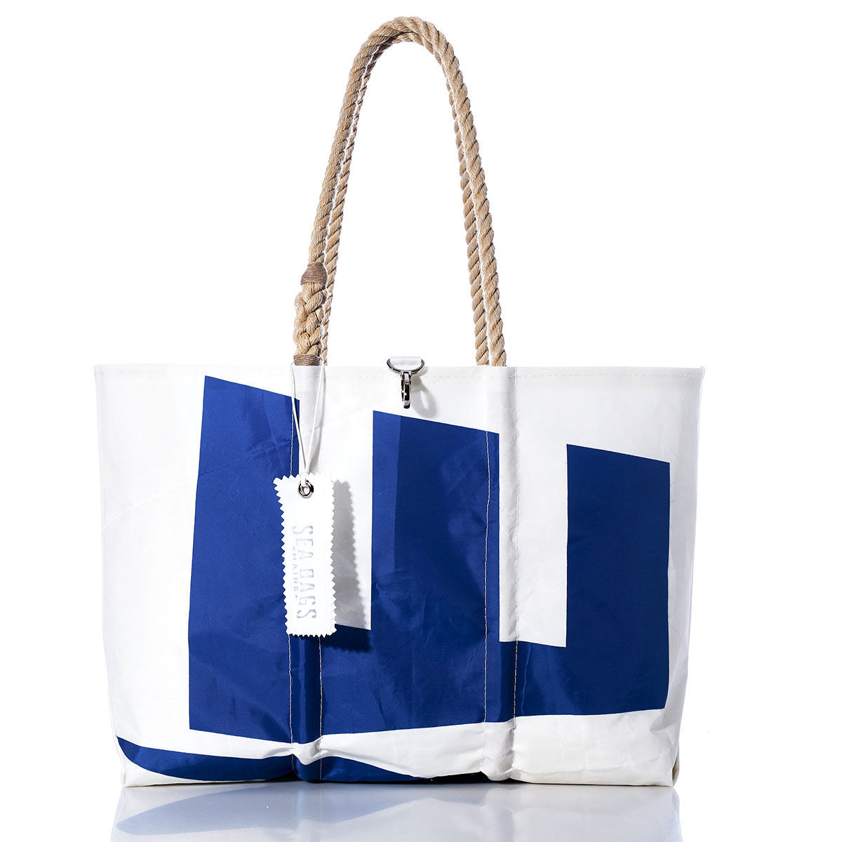 White tote bag featuring a bold blue geometric design, tan rope handles, and a white tag, photographed against a white background. This handmade Sea Bags tote—named the Vintage Etchells Large Tote—is inspired by classic sailing styles and offers timeless appeal for those seeking an iconic sailcloth bag. by Sea Bags