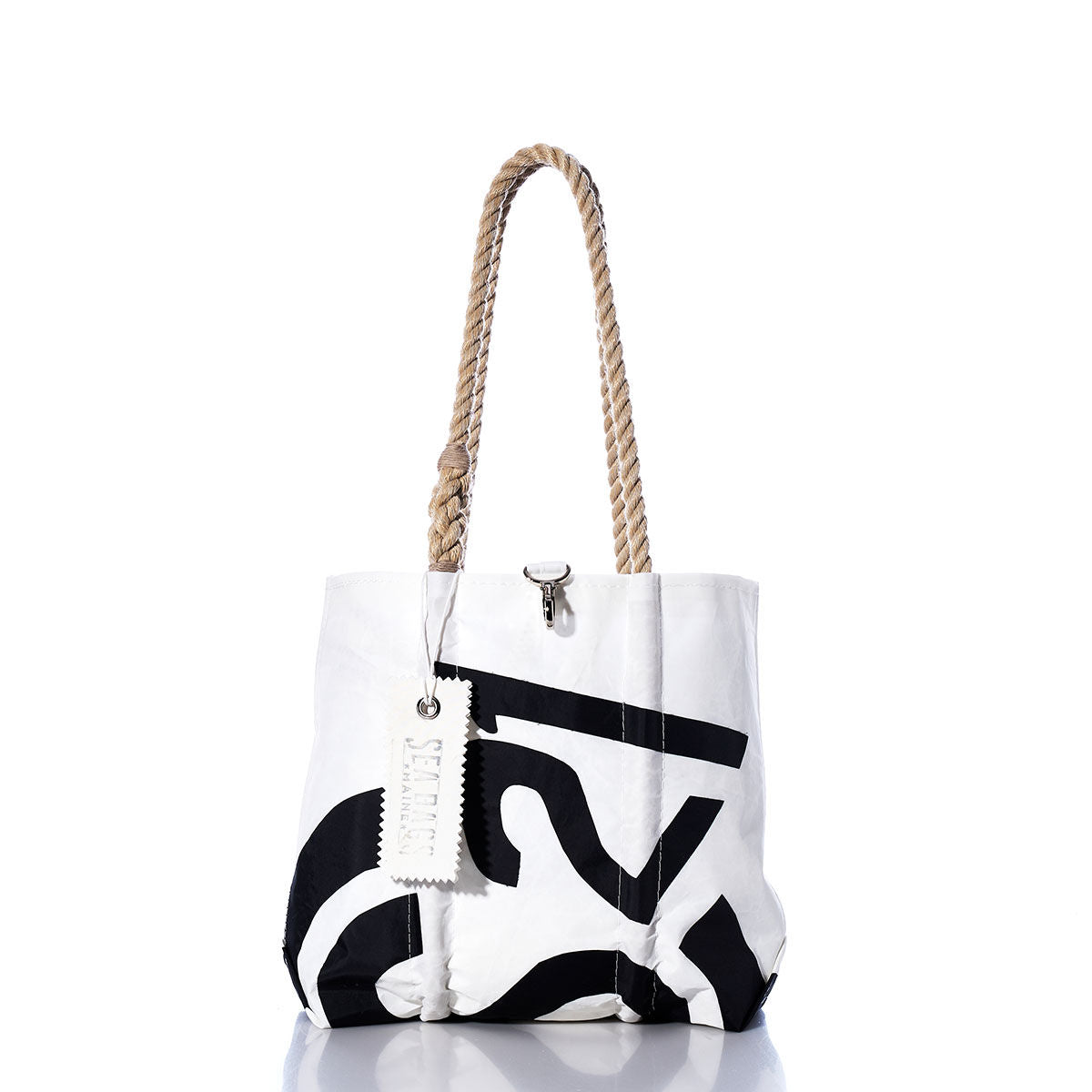 White tote bag with bold black print, hemp rope handles, and a white tag hanging from one handle, photographed on a white background with a subtle reflection below. The Sea Bags Vintage CS21 Handbag is inspired by classic sail insignias, blending timeless style with nautical flair. by Sea Bags