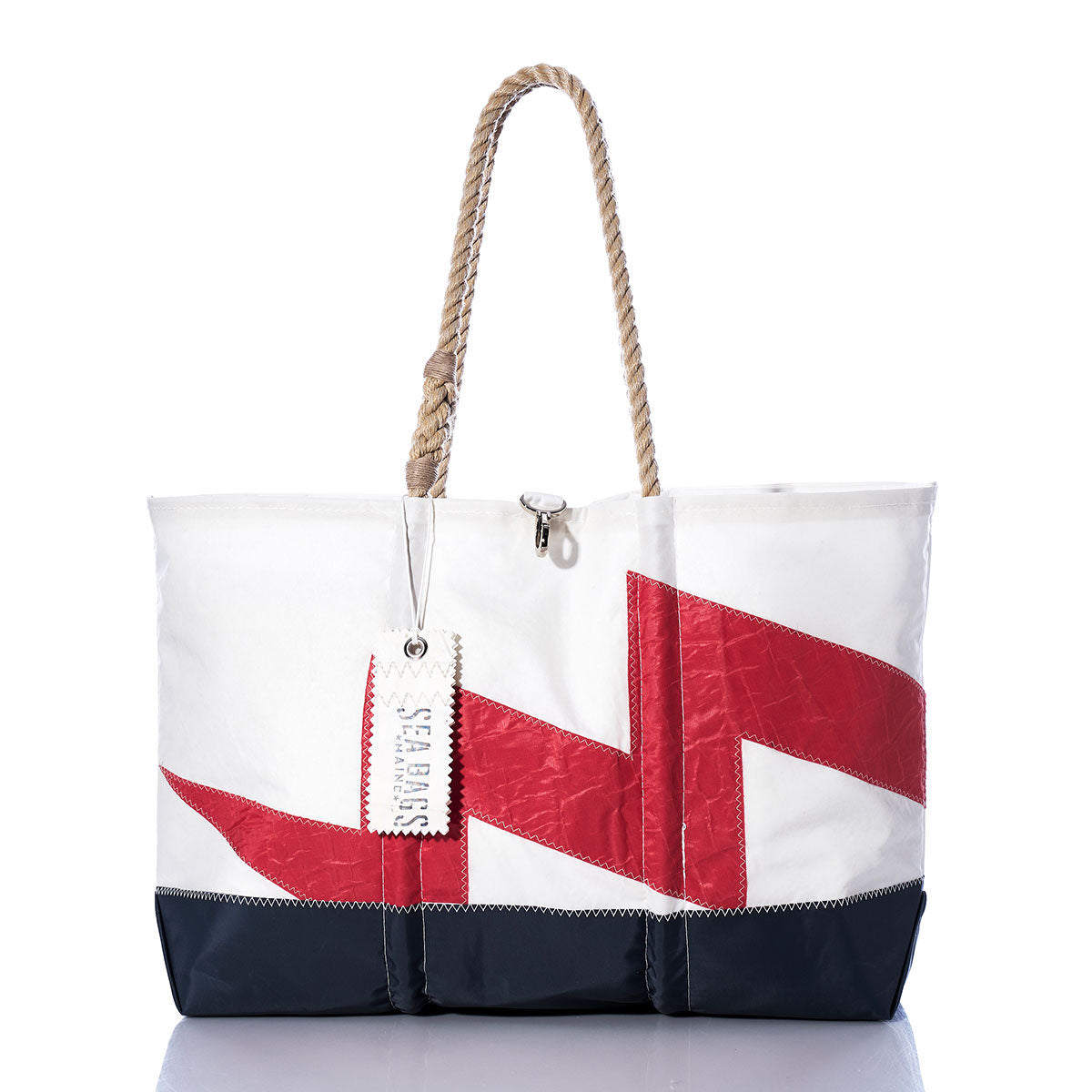 Vintage Lightning Ogunquit Beach Tote by Sea Bags in white and navy, featuring a red geometric design and crafted from recycled sail cloth with rope handles and a signature Sea Bags tag, photographed on a white background with a reflective surface. by Sea Bags