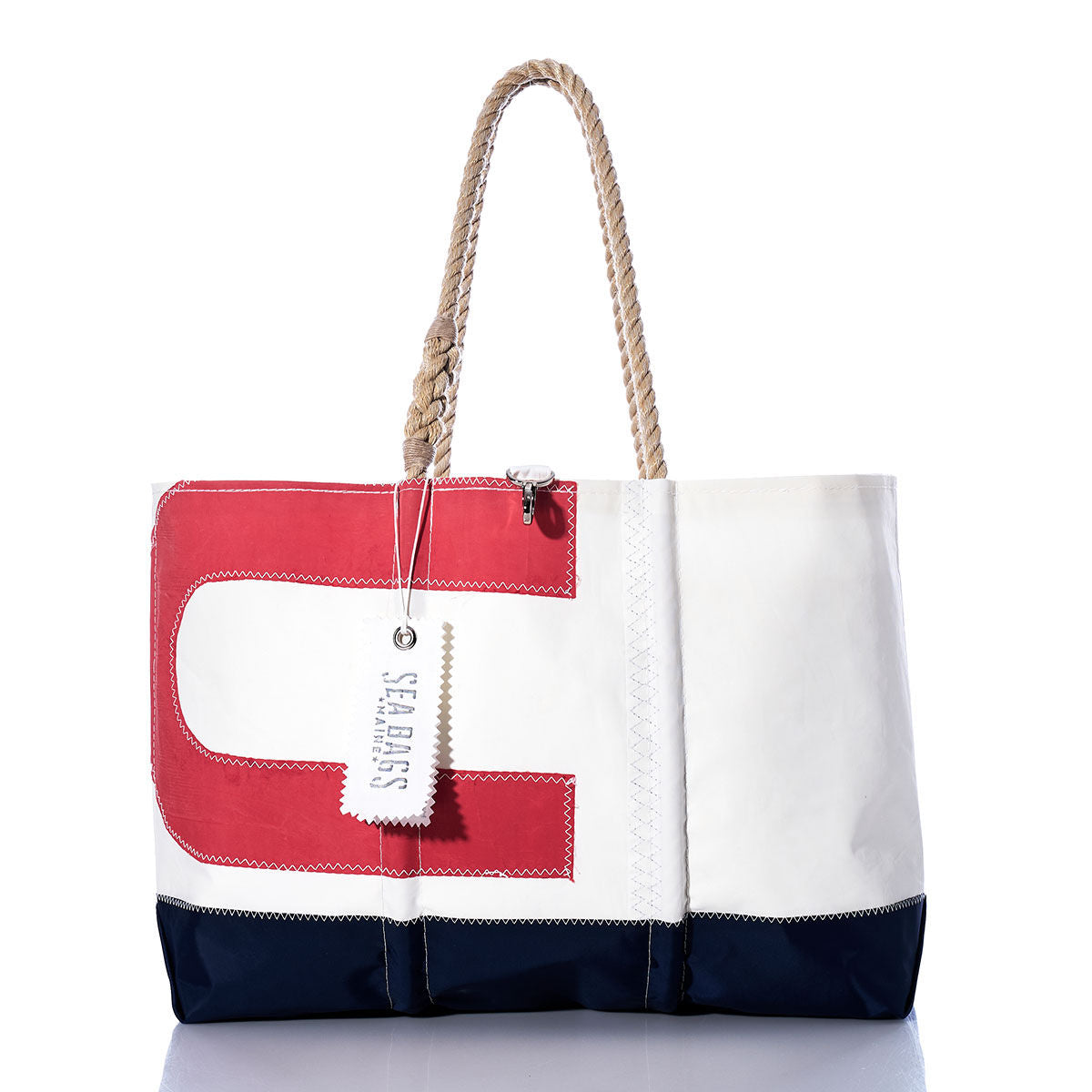 The Vintage USA Ogunquit Beach Tote by Sea Bags is a color-blocked tote in red, white, and navy, featuring sturdy rope handles and crafted from recycled sail cloth. It showcases a bold red letter C on the front along with an attached Sea Bags tag. The tote is displayed against a white background. by Sea Bags