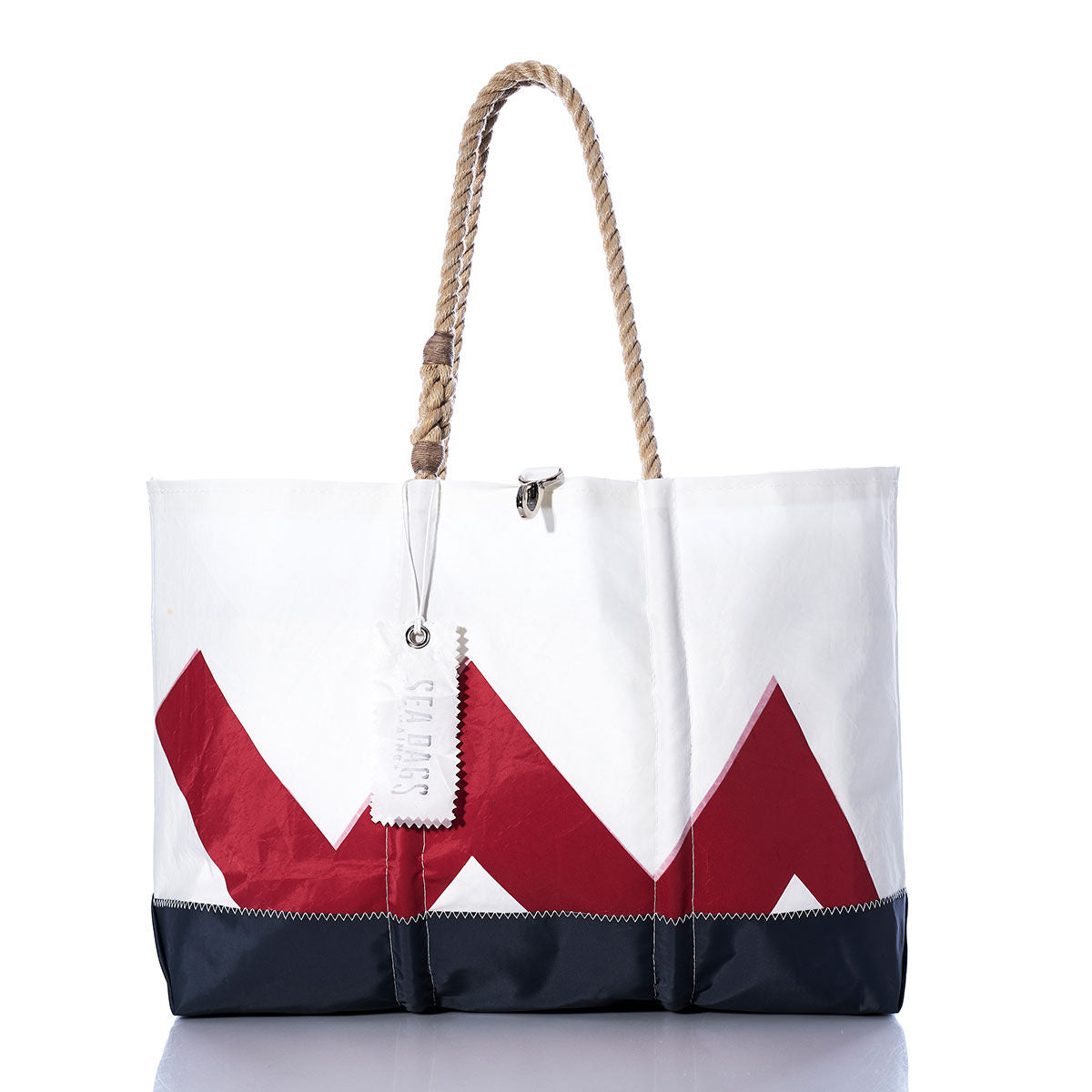 Vintage Lightning Ogunquit Beach Tote by Sea Bags, featuring a white recycled sail cloth with a bold red zigzag lightning design, navy blue bottom, sturdy rope handles, and a white Sea Bags tag. Shown on a white background with its reflection visible below. by Sea Bags