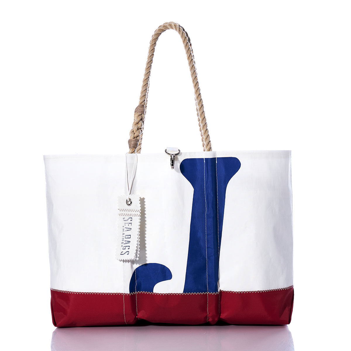 The Vintage J24 Ogunquit Beach Tote by Sea Bags features a striking white and red design with a blue anchor motif, rope handles, and a white tag near the top. Crafted from recycled sail cloth, this tote seamlessly blends style and sustainability for all your seaside adventures. by Sea Bags