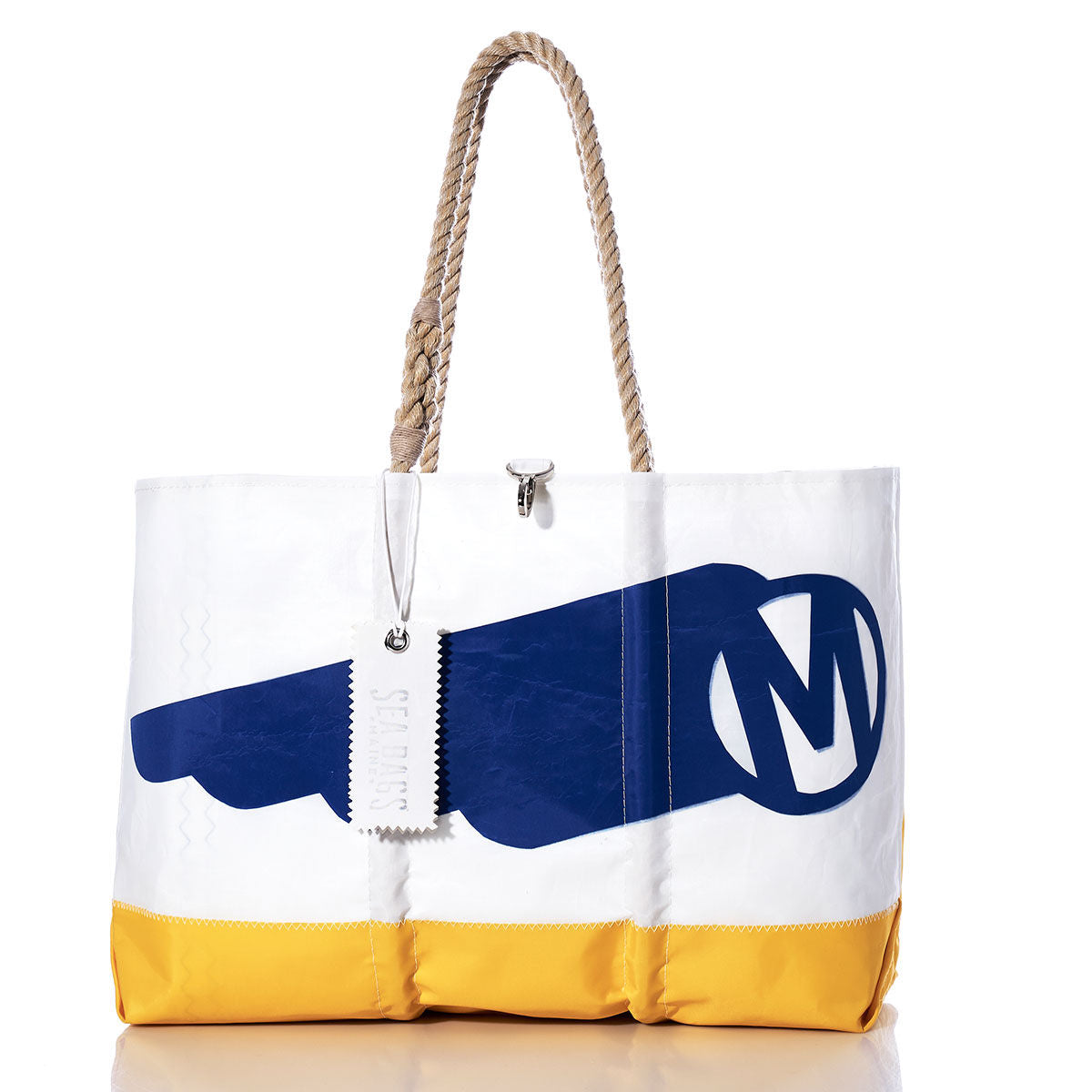 Sea Bags’ Vintage Mercury Ogunquit Beach Tote is a white recycled sail cloth bag with a yellow base, blue graphic featuring a large M in a circle inspired by vintage Mercury branding, durable rope handles, and a silver zipper pull engraved with “SMITHS.”. by Sea Bags