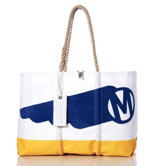 Sea Bags’ Vintage Mercury Ogunquit Beach Tote is a white recycled sail cloth bag with a yellow base, blue graphic featuring a large M in a circle inspired by vintage Mercury branding, durable rope handles, and a silver zipper pull engraved with “SMITHS.”. by Sea Bags