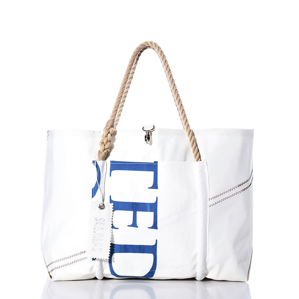 The Sea Bags Vintage TED Wharf Tote is a white recycled sail bag with rope handles, blue lettering on the side, a front pocket, and visible stitching details—showcased against a white background. Inspired by the iconic wharf tote and handmade in Portland, Maine. by Sea Bags