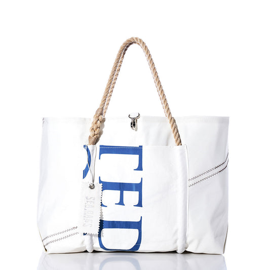 The Sea Bags Vintage TED Wharf Tote is a white recycled sail bag with rope handles, blue lettering on the side, a front pocket, and visible stitching details—showcased against a white background. Inspired by the iconic wharf tote and handmade in Portland, Maine. by Sea Bags