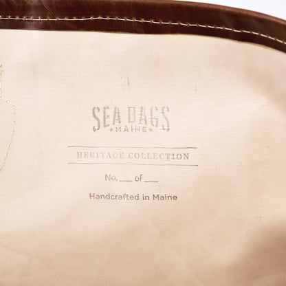 Certainly Here’s the revised sentence using your product data: A beige fabric label reads “SEA BAGS MAINE, HERITAGE COLLECTION, No. ___ of ___, Handcrafted in Maine,” with brown trim visible at the top—a subtle homage to classic yacht restoration traditions embodied by vessels like S/Y AELLO, which inspires the Sea Bags Heritage Aello Large Tote.