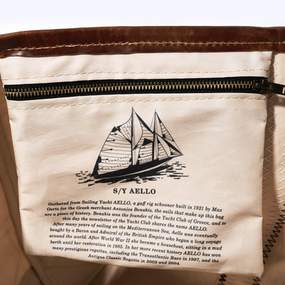 Close-up of a white fabric zippered pouch or bag with printed text and a sailboat illustration. The text references S/Y Aello and includes historical sailing details.