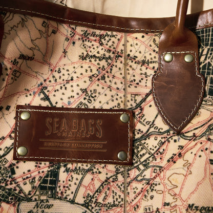 Close-up of the Sea Bags Heritage Aello Large Tote, featuring a map design, leather handle, and a leather patch embossed with “Sea Bags”—an ideal accessory for enthusiasts inspired by the classic yacht restoration traditions of the Greek sailing yacht S/Y AELLO.