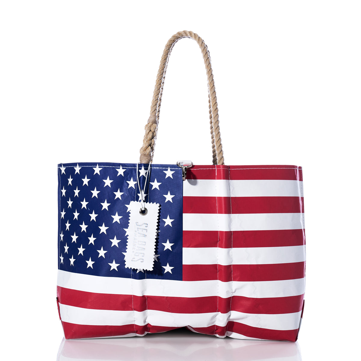Introducing the Vintage Limited Edition American Flag Large Tote by Sea Bags—a handcrafted in the USA tote, made from recycled sail cloth and featuring sturdy rope handles. Showcasing the iconic stars and stripes design, this spacious bag proudly displays a white “Sea Bags” tag hanging from one of its handles.