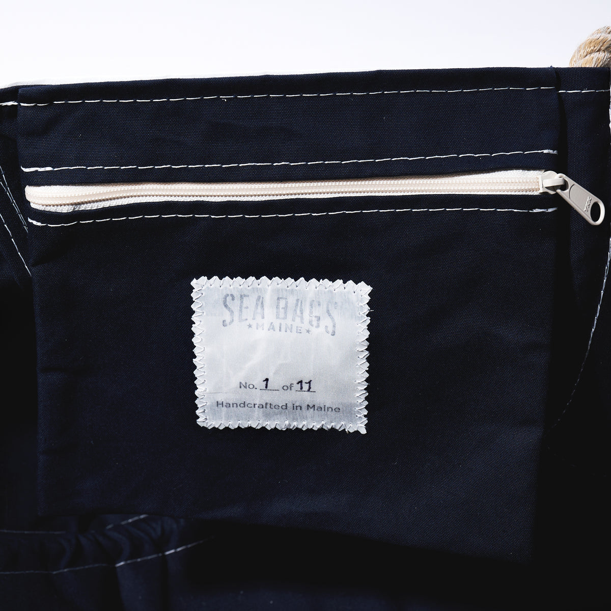 Close-up of a dark navy blue fabric bag with white stitching, a cream zipper, and a white brand label reading Sea Dogs Nails.