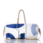 The Sea Bags Vintage 12 Duffel, crafted from recycled sail cloth in white and blue, features sturdy hemp rope handles, a beige shoulder strap, and a white tag. It is displayed on a reflective surface against a white background. by Sea Bags