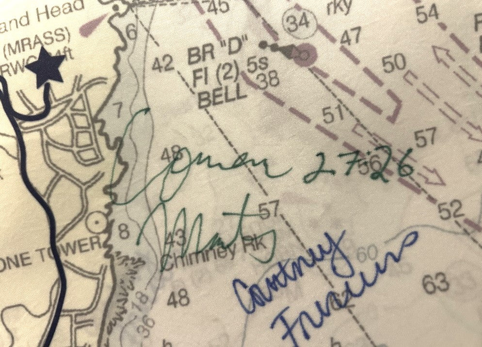 A close-up of a nautical chart featuring multiple handwritten signatures in green and blue ink—including Connor 2.7.26, Matt, and Courtney Frauden—captures the spirit of the Maine coast. Evoking memories of local traditions like the Beach to Beacon 10K, this scene highlights sustainable practices found in Sea Bags’ Auction TD Beach to Beacon Mile Marker 6.2 Tote, crafted from recycled sail cloth and cherished by coastal communities. by Sea Bags