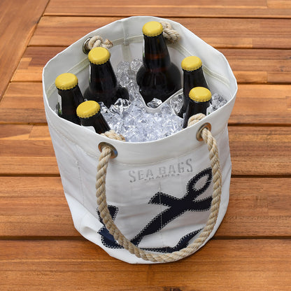 The Navy Anchor Beverage Bucket Bag by Sea Bags, crafted from recycled sail cloth, features rope handles and holds ice and six brown beer bottles with yellow caps, displayed on a wooden surface. by Sea Bags