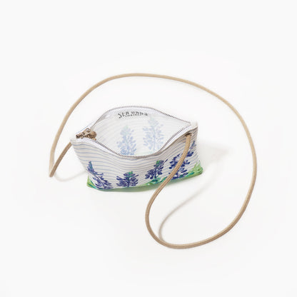 The Lupine Sailor Stripe Slim Crossbody by Sea Bags is a small zippered pouch crafted from recycled sail cloth with a blue and green lupine floral print on a white background, complemented by a beige strap. The pouch is shown open, revealing a matching patterned lining inside. by Sea Bags
