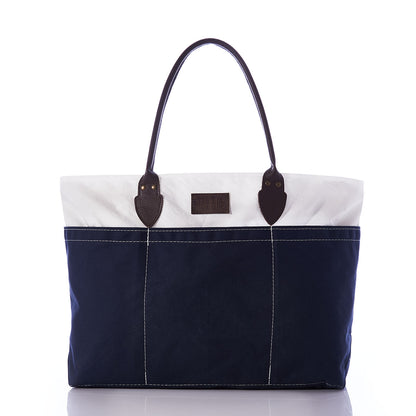 The Chebeague Large Travel Tote by Sea Bags is a spacious, water-resistant canvas bag featuring dark handles, a white upper section, and a navy blue lower section, showcased against a white background. by Sea Bags