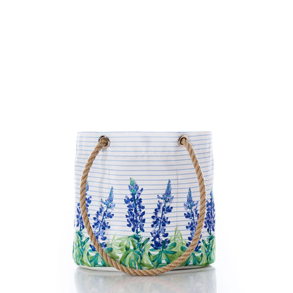 Introducing the Sea Bags Lupine on Sailor Stripe Essential Handbag—a white tote featuring a captivating blue floral lupine design over classic horizontal sailor stripes. Crafted from recycled sail cloth for an eco-friendly touch, this lightweight and practical handbag boasts two sturdy rope handles. Perfect for everyday use and displayed elegantly against a white background. by Sea Bags