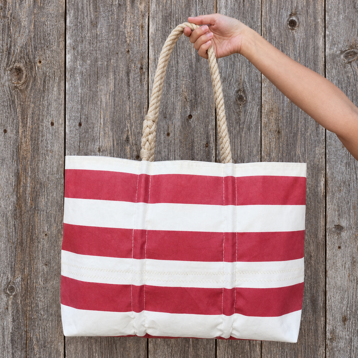 A hand holds a large, striped Red Rugby Stripe Large Tote by Sea Bags with thick rope handles.