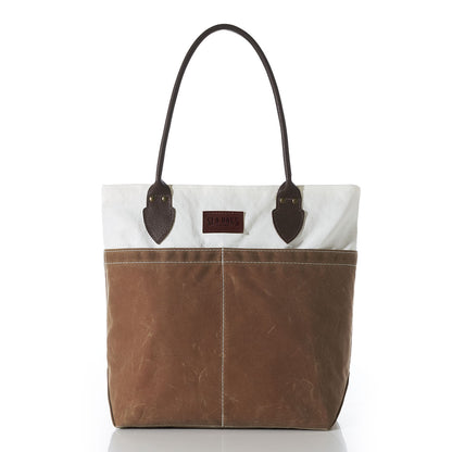 A Sea Bags Tan Chebeague Tote, showcasing dark brown leather handles, a white upper section crafted from recycled sail cloth, and a tan lower section made of durable waxed canvas, photographed against a white background. by Sea Bags