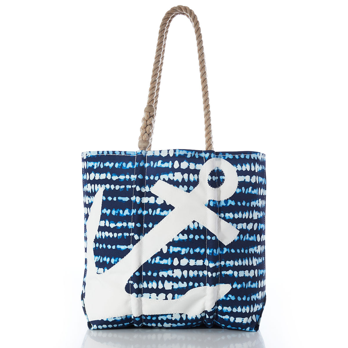 The Sea Bags White Anchor on Shibori Print Tote features a navy blue shibori-inspired patterned background, a white anchor design, and braided rope handles, shown standing upright on a white surface. by Sea Bags
