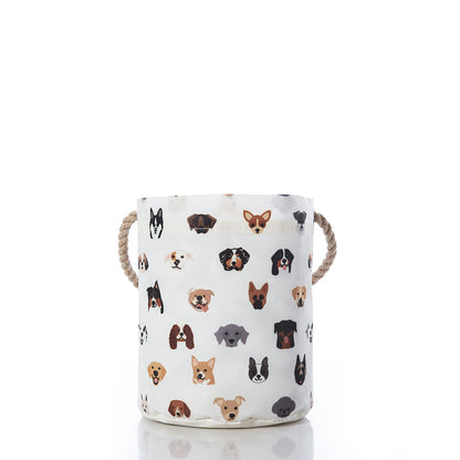 The Sea Bags Popular Pups Print Bucket Bag is a white fabric dog storage basket featuring sturdy rope handles and decorated with colorful cartoon dog faces of various breeds on a plain white background. This delightful pet organizer helps keep your furry friends toys tidy while adding a playful touch to any room. by Sea Bags